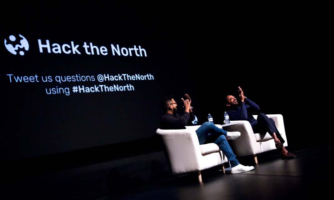 Two speakers sitting in armchairs onstage at Hack the North