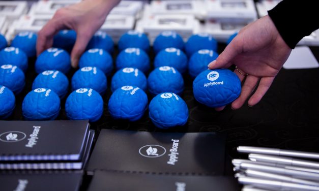 Blue brain-shaped stress balls with Applyboard's logo on them beside notebooks on a table