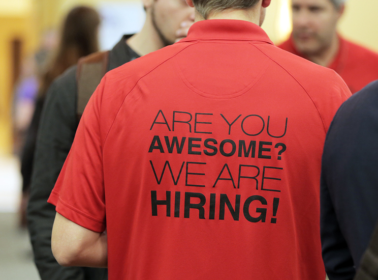 Individual wearing a red shirt. The back reads: "Are you awesome? We are hiring!"